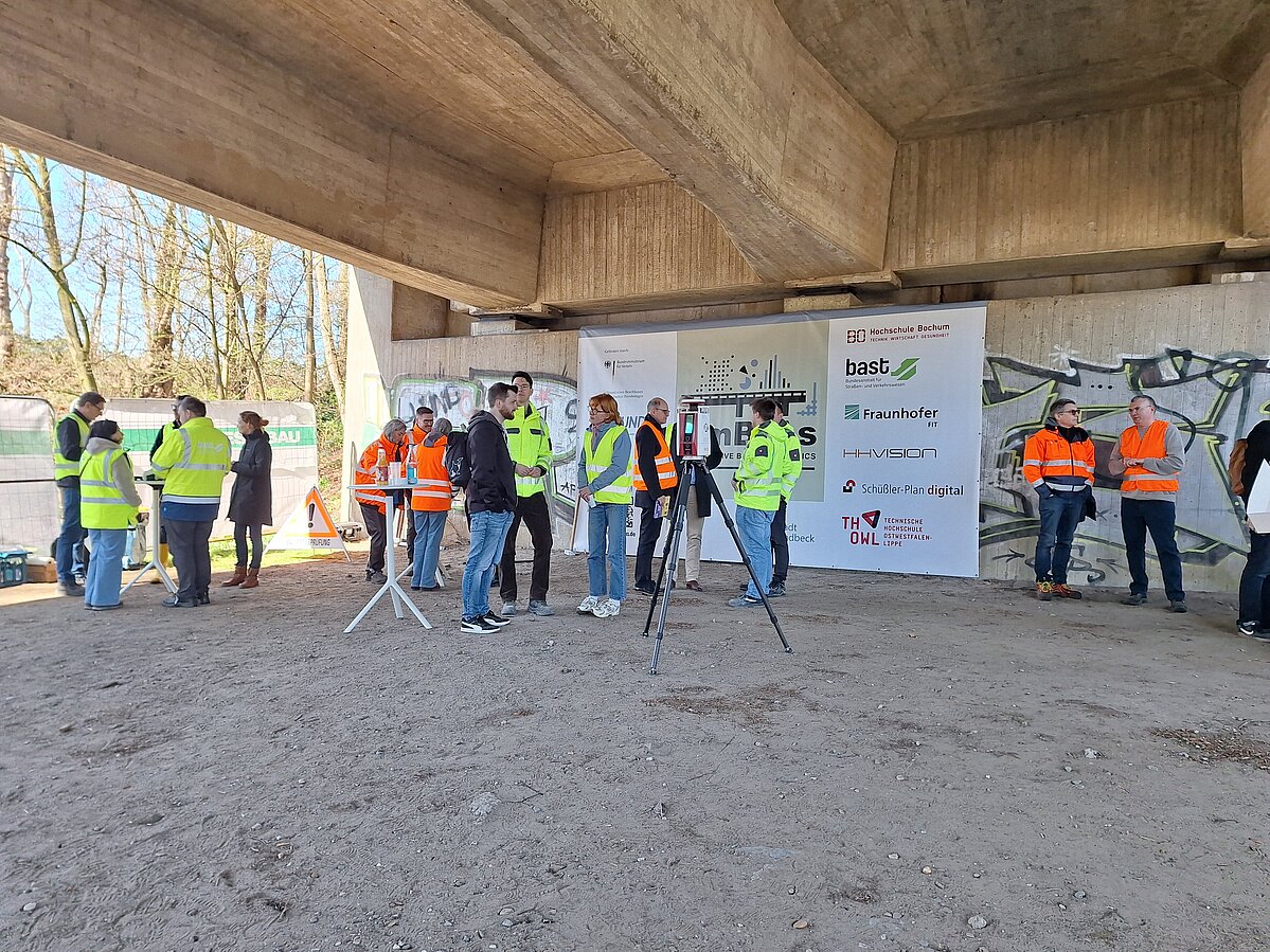 Eine Gruppe von Menschen diskutiert, analysiert unter einer Betonbrücke deren Beschaffenheit