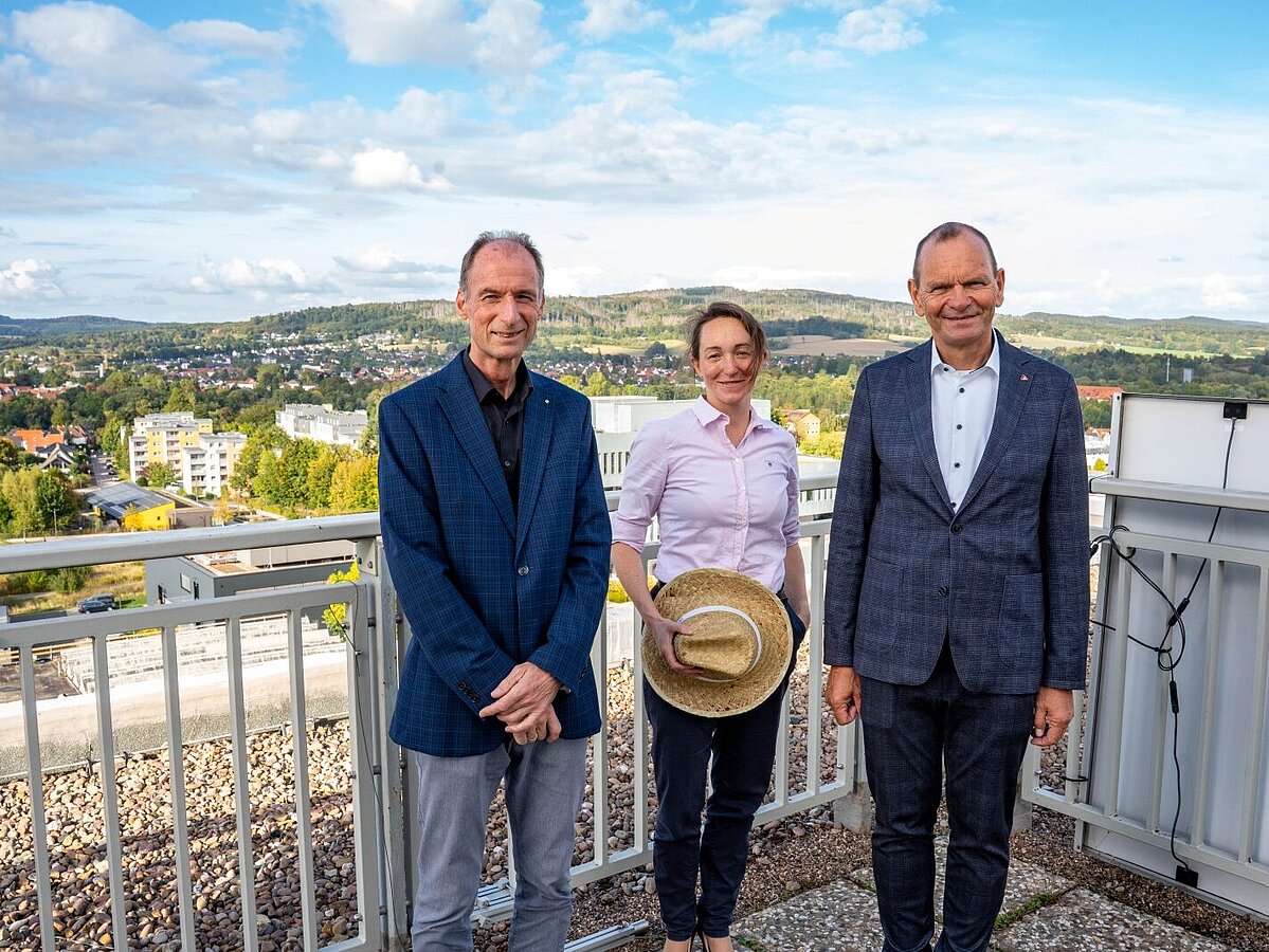 Two men and a woman are standing in front of a railing on a roof terrace. In the background, you can see the Innovation Campus Lemgo.