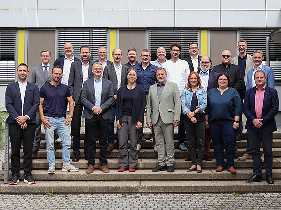 Gruppenfoto: Versetzt auf einer Treppe in drei Reihen stehen 18 Männer und drei Frauen und blicken in die Kamera.