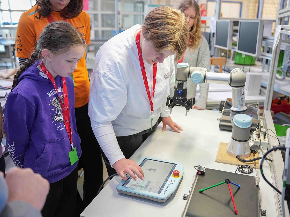 Eine Gruppe von Mädchen begutachtet einen Roboter. Eine von ihnen nimmt Einstellungen an einem Ipad vor.
