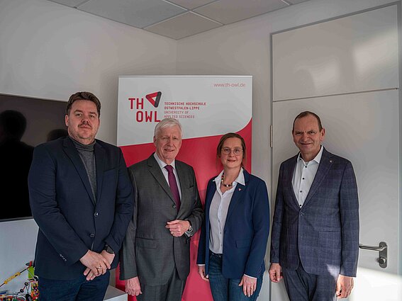 Foto: Drei Herren und eine Dame stehen in einem Büro und blicken freundlich in die Kamera. 