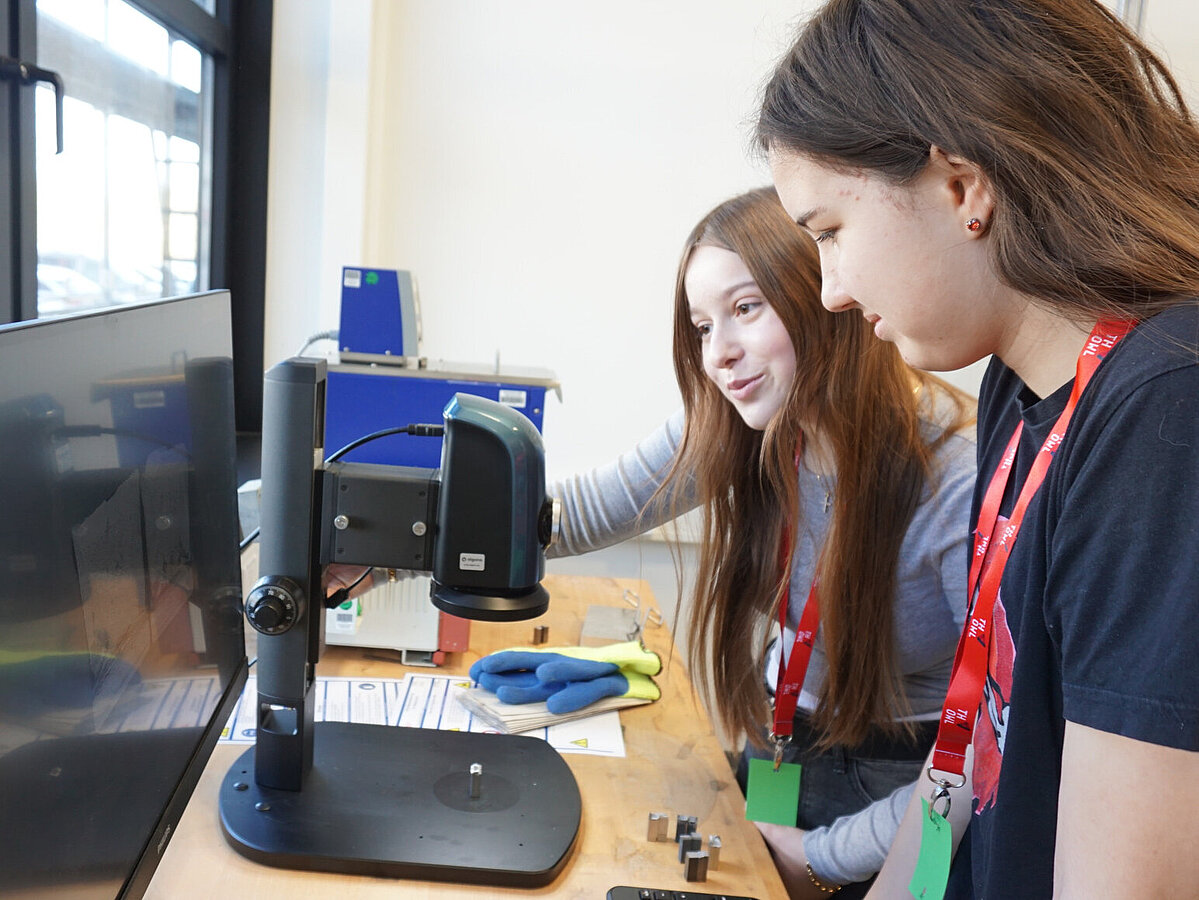 Zwei Schülerinnen schauen sich auf einem Computer die Ergebnisse des Experiments an. 