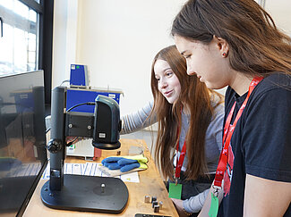 Zwei Schülerinnen schauen sich auf einem Computer die Ergebnisse des Experiments an. 