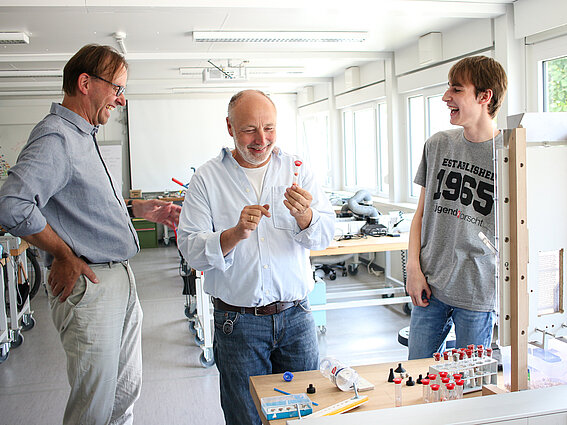 Rainer Kammler from the TechLipp Learning Lab (center) is holding a small hourglass. He is talking with Tim Kammel (right) and Dr. Jens Schulze (left). The student lab can be seen in the background.