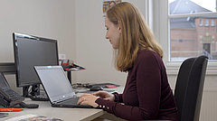 Frau sitzt am Schreibtisch und arbeitet am Laptop