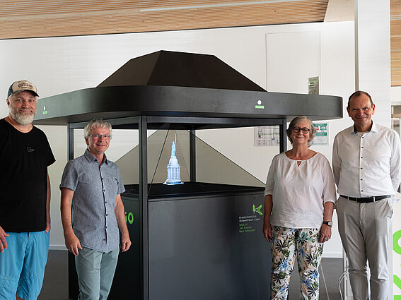 Von rechts: Professor Dr. Jürgen Krahl, Professorin Dr. Edeltraud Vomberg, Professor Dr. Guido Falkemeier und Jan Pieniak stehen vor einer Hologrammvitrine im KreativInstitut.OWL 