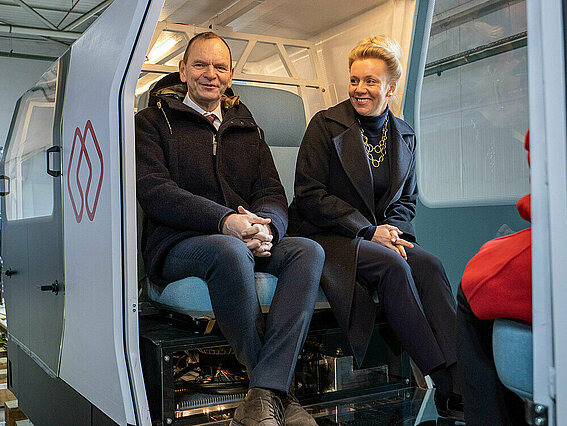 Wissenschaftsministerin Ina Brandes und TH OWL-Präsident Professor Dr. Jürgen Krahl fahren in der Testhalle in Dörentrup-Humfeld mit dem MONOCAB