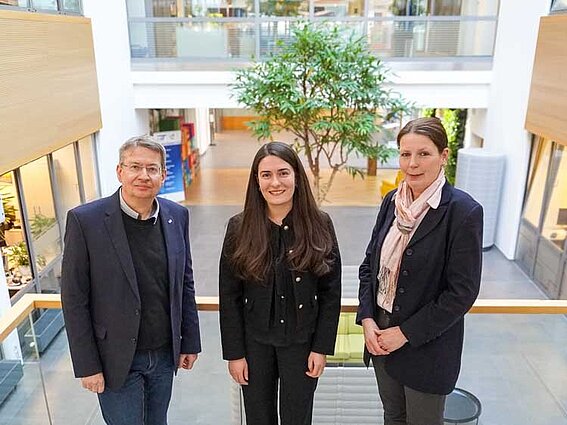 Foto: Ein Mann und zwei Frauen blicken nebeneinander stehend in die Kamera.