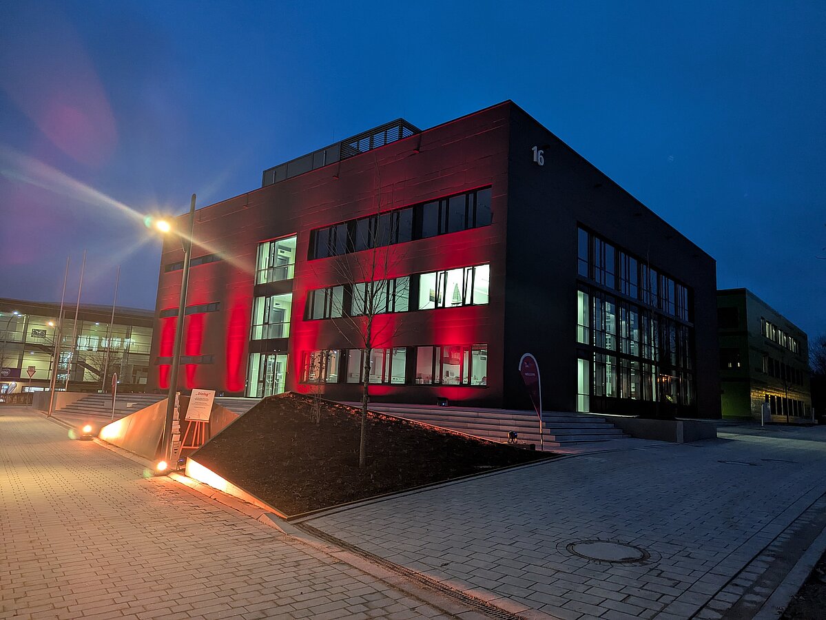 Nachaufnahme eines rot angestrahlten Laborgebäudes mit Kunstwerk im Vordergrund.