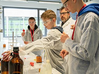 Drei jungen im Kittel arbeiten und ein Dozent analysieren Proben im Labor.