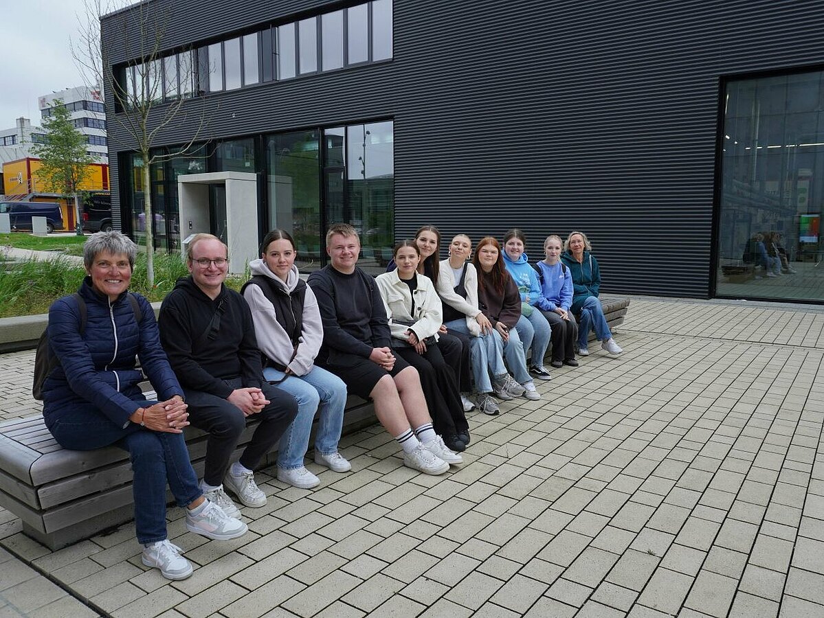 Eine Gruppe von Schülerinnen und Schülern und Lehrerinnen und Lehrer sitz auf Bank vor dem Gebäude Future Food Factory der TH OWL