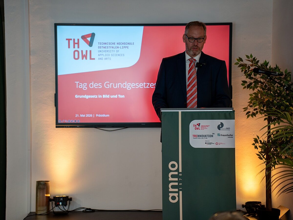Professor Dr. Florian Hobbeling hält beim „Tag des Grundgesetzes 2026“ der TH OWL einen Vortrag am Rednerpult. Im Hintergrund ist die Präsentation zur Veranstaltung zu sehen.