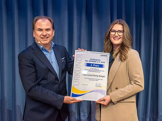 Ein Mann und eine Frau halten eine Urkunde in der Hand und posieren für ein Foto.