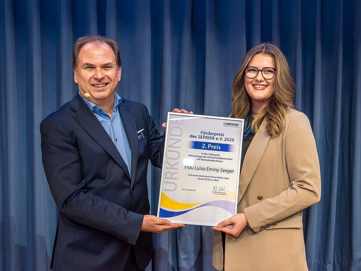Ein Mann und eine Frau halten eine Urkunde in der Hand und posieren für ein Foto.