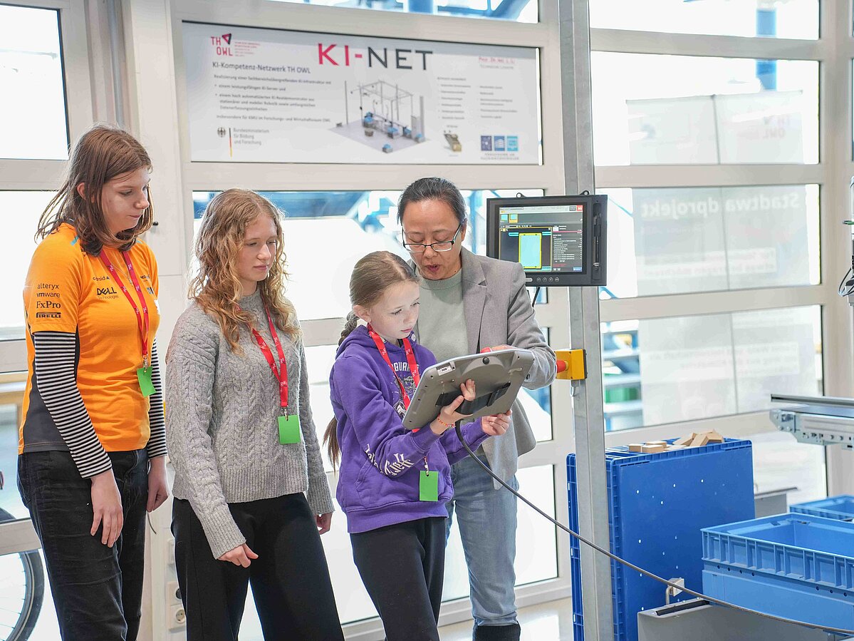 Eine Frau erklärt drei Mädchen die Einstellungen eines Roboters auf dem Ipad.