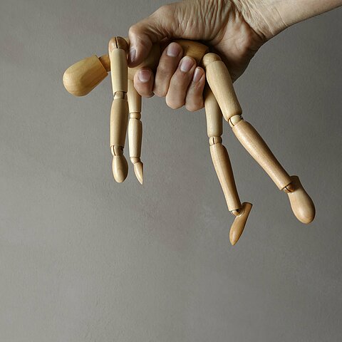 Eine Hand hält eine Holzpuppe und formt dabei eine Faust.