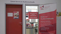 Rote Eingangstür des Career-Service mit einem Roll-Up mit Informationen zu den Kursen zur Studienmethodik daneben