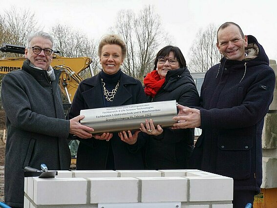 Wolfgang Feldmann (Niederlassungsleiter BLB NRW), Ina Brandes (Ministerin für Kultur und Wissenschaft des Landes NRW), Gabriele Willems (Geschäftsführerin BLB NRW) und Prof. Dr. Jürgen Krahl (v.l.) versenken die Zeitkapsel im Grundstein eines Laborneubaus.