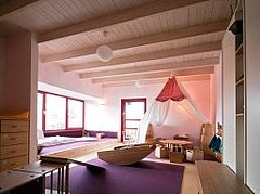 Innenraum der Kita Sterntaler mit einer Holzwippe, einem Gruppentisch und Stühlen aus Holz und einem weißen Himmel darüber