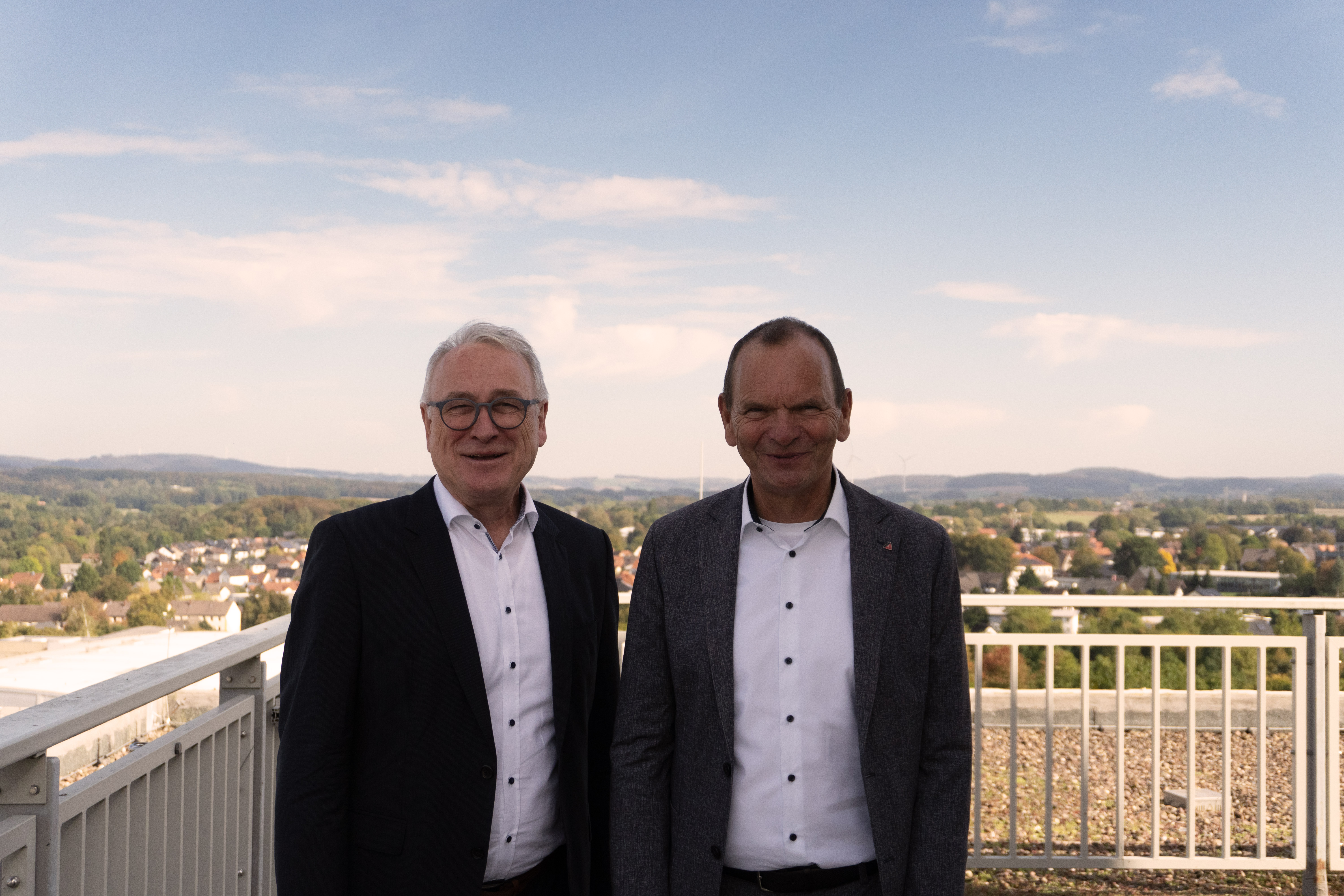 Foto: Zwei Männer stehen auf einer Terasse und lächeln in die Kamera. 